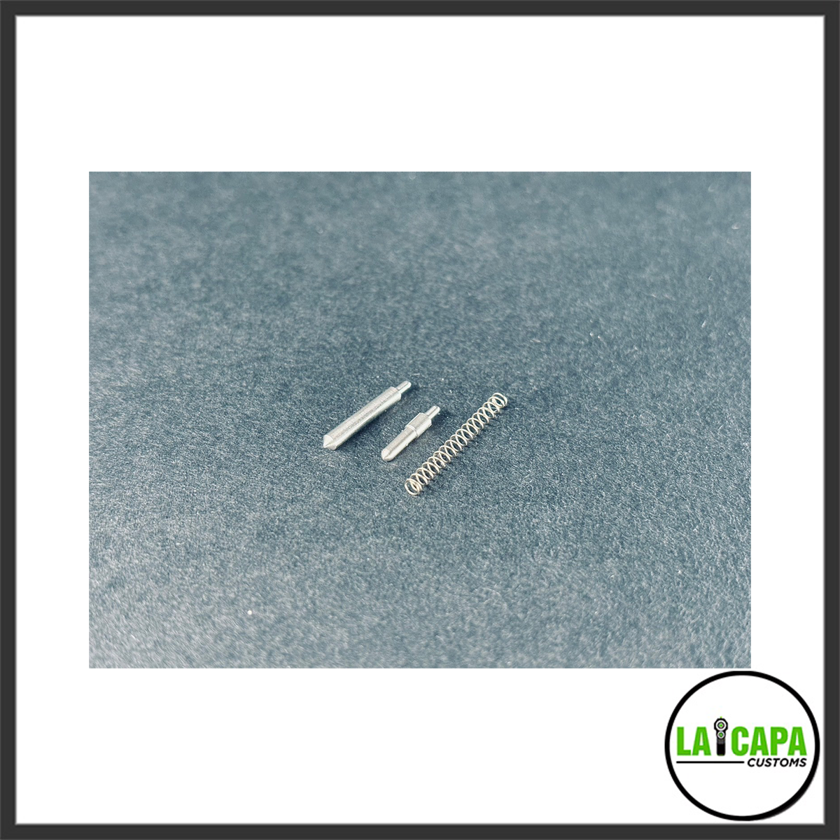 Two small metal detent pins and a coil spring laid out on a grey surface, shown as included hardware components.
